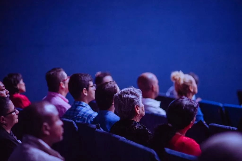 Un grupo de personas, entre ellas varias mayores de 65 años, en una sala de cine disfrutando de la proyección de una película.